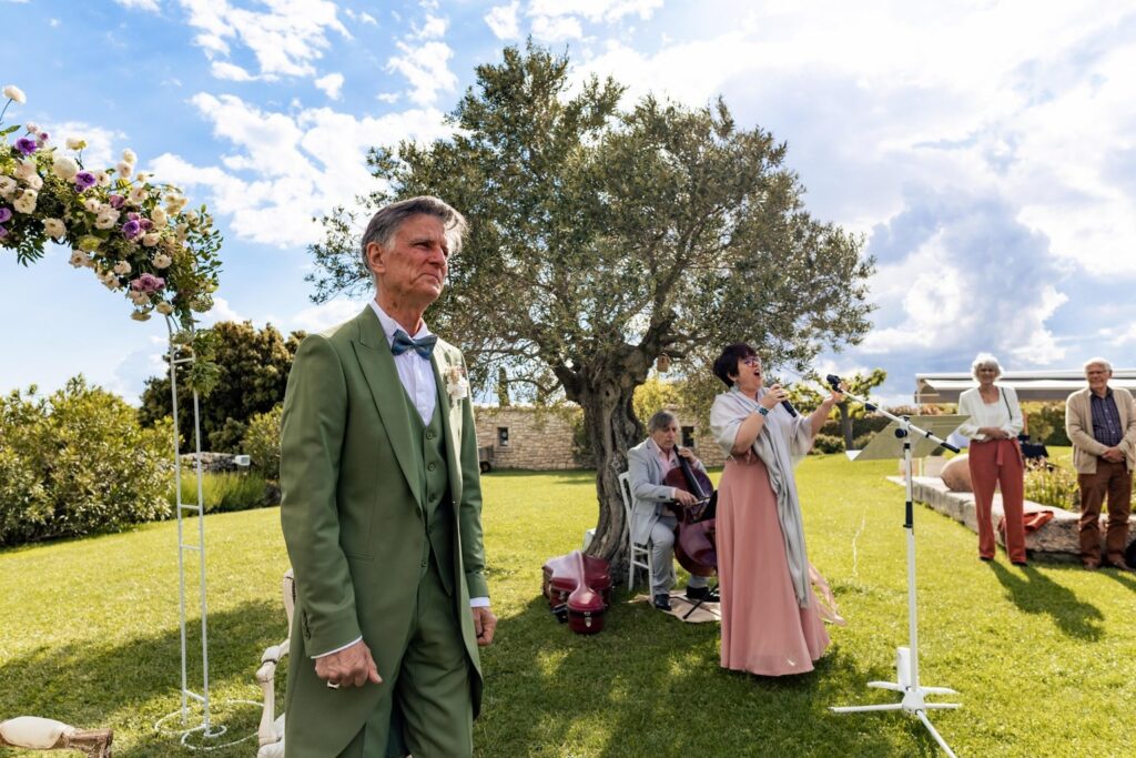 Chanteuse accompagnée d’un violoncelliste lors d’une cérémonie de mariage en plein air, sous un olivier.